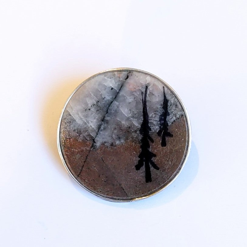 Thin sliver of rock forms this brooch, with trees painted on, created by Wendy Stanwick of A Slice of the North. Jewellery.